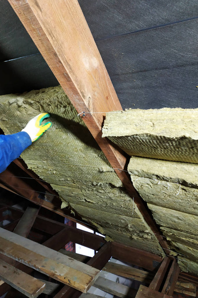Un homme installe une couche d'isolation thermique d'un toit thermique à l'aide de panneaux de laine minérale, le montant entre les poutres du toit de la maison pour se réchauffer du froid
 - Photo, image