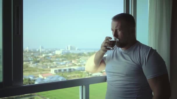 männlich trinkt kaffee und blickt durch panoramafenster lächelt morgens, zeitlupe - Filmmaterial, Video
