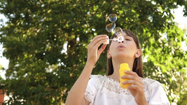 šťastná dívka foukání krásné mýdlové bubliny v parku na jaře, v létě a s úsměvem. Zpomalený pohyb. mladá dívka projíždějící městem v parku. - Fotografie, Obrázek
