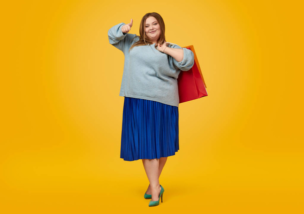 Plus size woman with paper bags gesturing thumb up - Zdjęcie, obraz