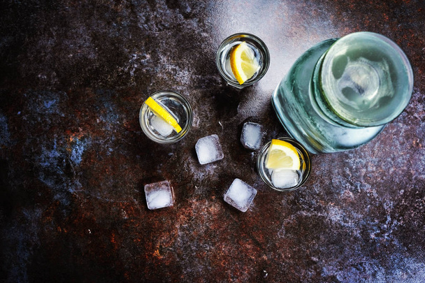 Wodka in glazen met citroen en ijs. Op de zwarte stenen tafel. Copyspace. - Foto, afbeelding