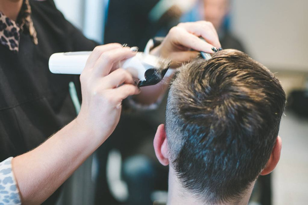 Парикмахер стрижет волосы мужчине электрическим триммером
 - Фото, изображение