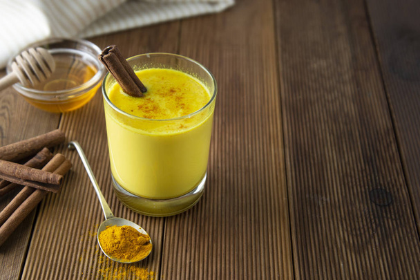 Turmeric Golden Milk. Healthy drink made with turmeric honey and cinnamon. Remedy for many diseases. Rustic wooden background. - Foto, imagen