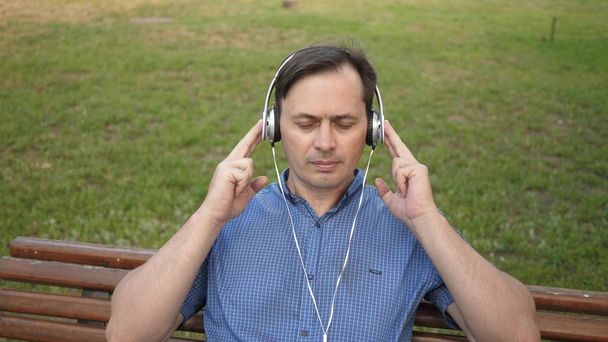 pohledný mladý muž v parku, poslech hudby ze svého smartphonu se sluchátky a tancování venku v parku na lavičce v centru Evropy. - Fotografie, Obrázek