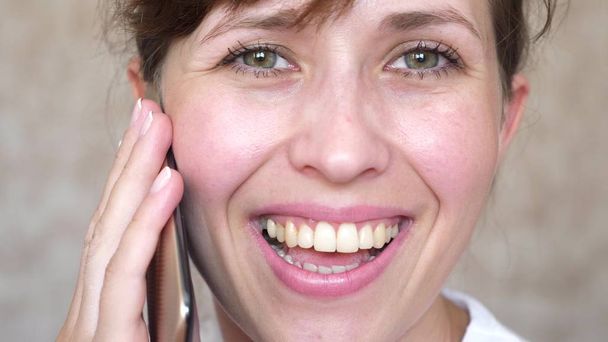 girl talking on a cell phone laughs, teeth closeup. woman talking on the smartphone and smiling close-up. need to brush your teeth. - Photo, Image