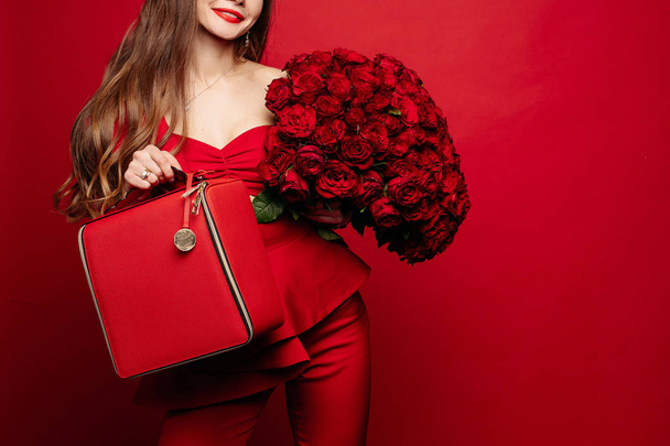Tyylikäs upea brunette punainen punaisia ruusuja ja punainen laukku
. - Valokuva, kuva
