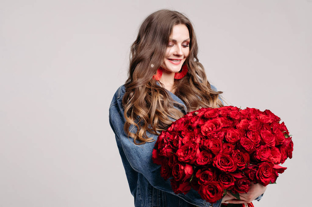 Superbe femme avec de gros boucles d'oreilles tenant des roses et souriant
. - Photo, image