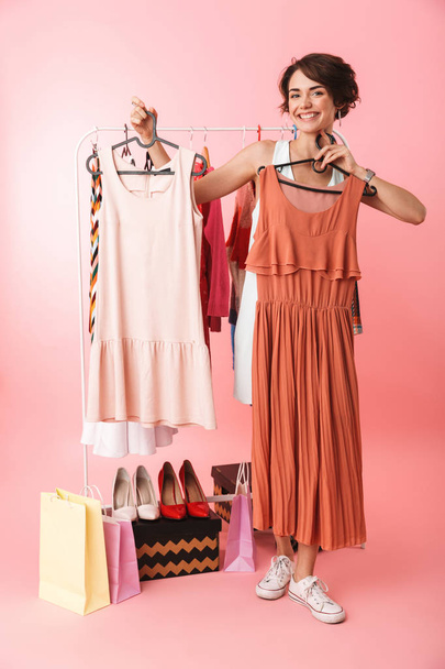 Woman stylist posing isolated over pink wall background near a lot of clothes. - 写真・画像