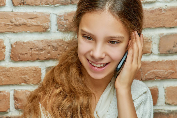 Усміхнена дівчина-підліток з довгим волоссям розмовляє на мобільному телефоні
 - Фото, зображення