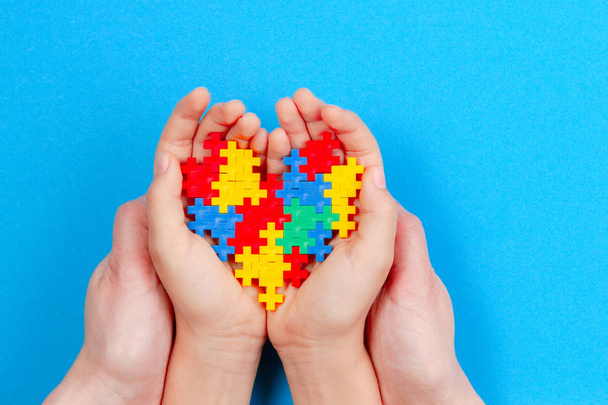 Adult and kid hands holding colorful heart on blue background. World autism awareness day concept - Photo, Image