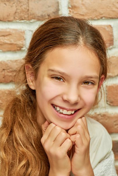 Дівчина-підліток з довгим волоссям посміхається на стіну
 - Фото, зображення