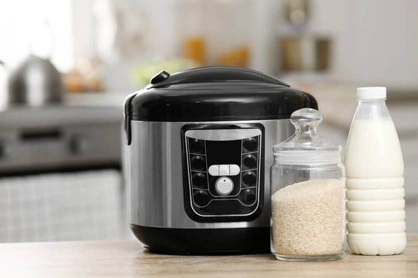 Modern electric multi cooker, rice and milk on table in kitchen - Фото, изображение