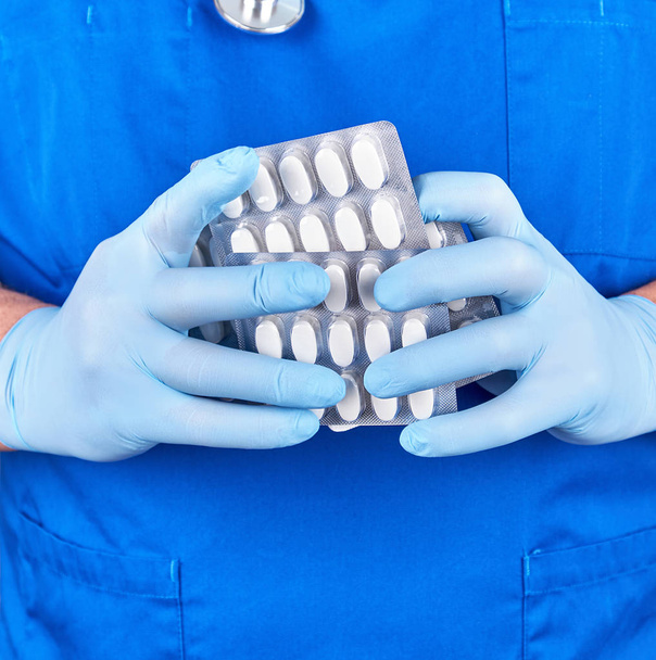 lekarz w niebieskim mundurze i sterylnych rękawicach posiadających białe tabletki w - Zdjęcie, obraz