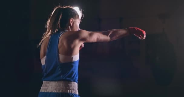 Prachtige vrouwelijke bokser voert een strijd met schaduw tijdens het sporten in de sportschool. Slow-motion. Steadicam schot - Video