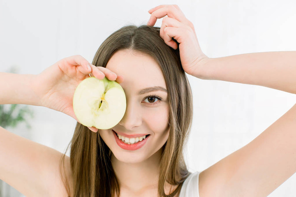 Smiling beauty woman holding half of green apple. The girl closes one eye with half an apple. - Фото, зображення