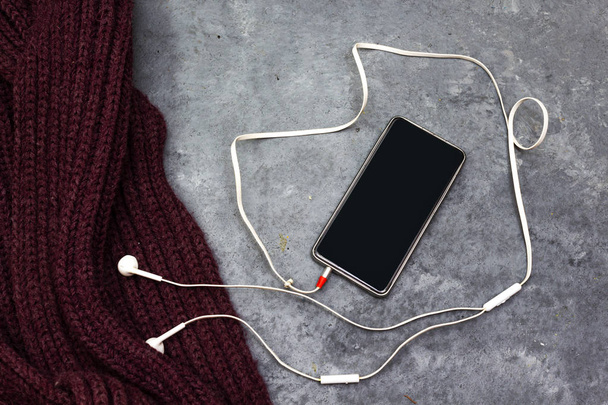 Creative flat lay photo of workspace desk with earphones and mobile phone above purple winter Woolen scarf - Photo, Image