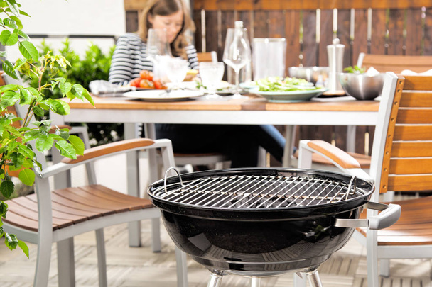 close-up view of black outdoor grill and young woman sitting and eating behind - Фото, зображення