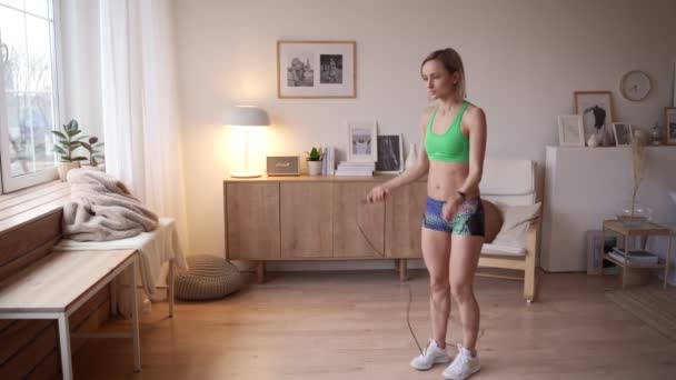 Cute young girl jumping rope at home enjoying the beautiful view from the window. The concept of achieving results and a healthy lifestyle - Materiał filmowy, wideo