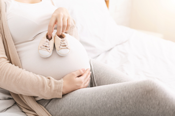 Petites chaussures pour bébé à naître sur le ventre de la femme enceinte
 - Photo, image