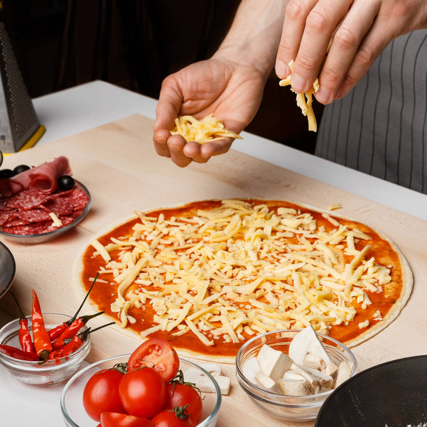 Prozess der Herstellung von Pizza. Koch fügt Käse auf Pizzaboden hinzu - Foto, Bild