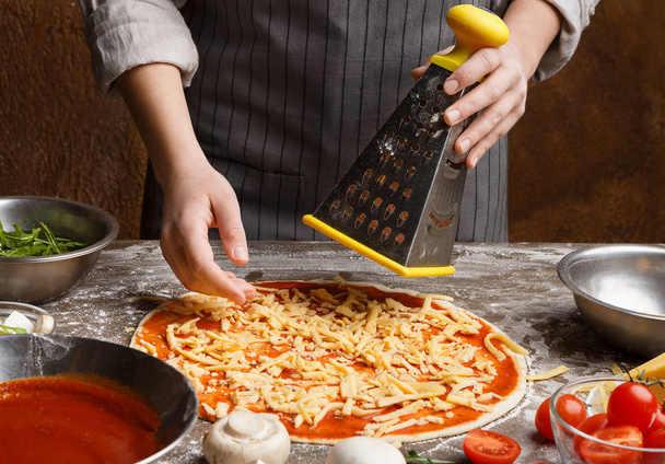 Preparing pizza. Woman rubbing cheese on grater - Photo, Image
