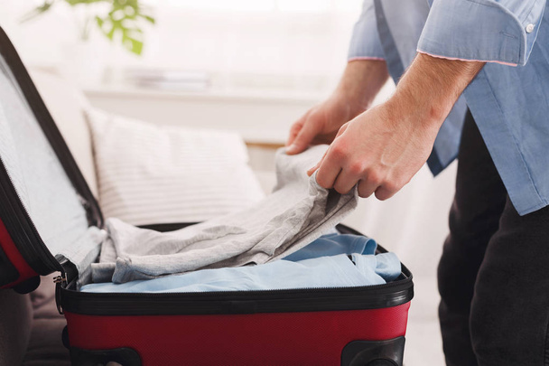 Young man packing suitcase on bed, closeup - Photo, image