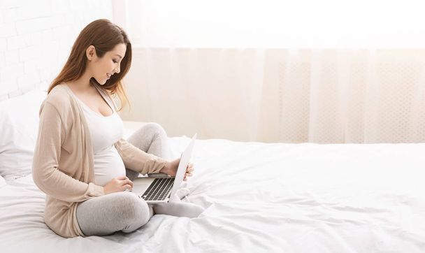 Hamile kadın yatakta onu laptop ile rahatlatıcı sevimli - Fotoğraf, Görsel