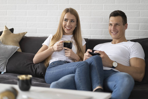 Νεαρό ζευγάρι να περνάει χρόνο μαζί στο σπίτι πίνοντας καφέ και μιλώντας. - Φωτογραφία, εικόνα