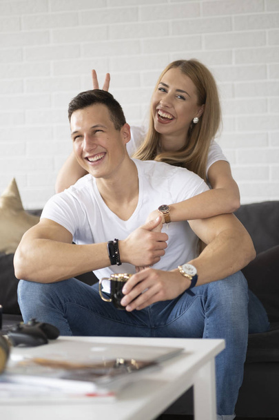 Νεαρό ζευγάρι να περνάει χρόνο μαζί στο σπίτι πίνοντας καφέ και μιλώντας. - Φωτογραφία, εικόνα