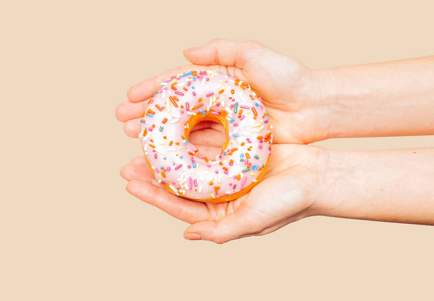 Female hands holding colorful donut on pastel background - Φωτογραφία, εικόνα