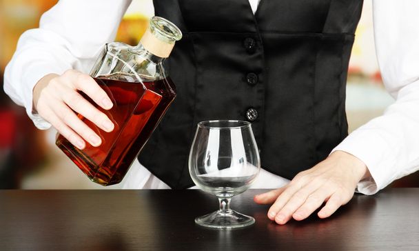 Barman hand with bottle of cognac pouring drink into glass, on bright background - Φωτογραφία, εικόνα