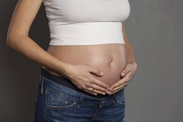 Raskaana olevan naisen vatsa. Toimikausi 6 kuukautta, lähikuva. Harmaa tausta
 - Valokuva, kuva