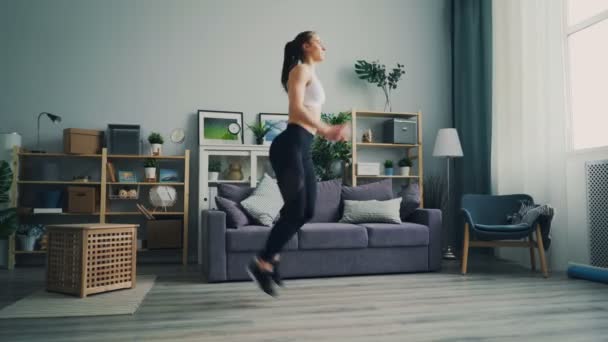 Slim young lady focused on running on the spot exercising in light apartment. - Materiaali, video