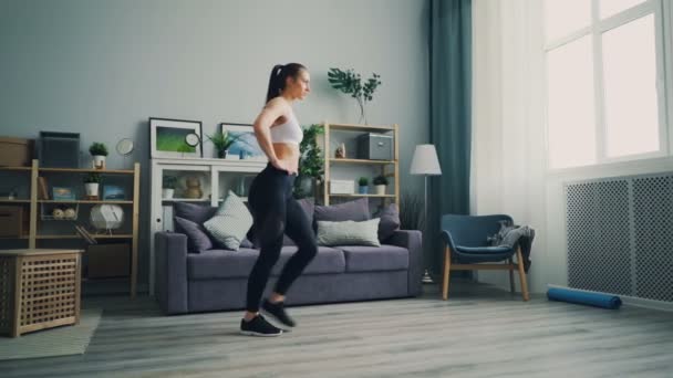 Pretty female student doing sports at home crouching enjoying healthy lifestyle - Záběry, video