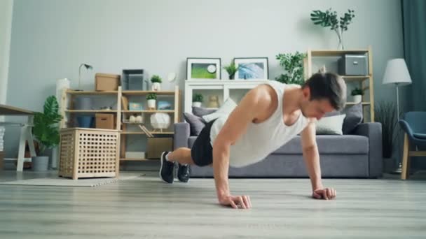 Muscular dark-haired guy doing pushup working out at home in comfortable clothes - Πλάνα, βίντεο