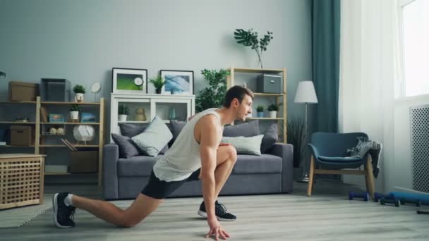 Good-looking young man in sportswear doing exercises at home stretching legs - Filmagem, Vídeo