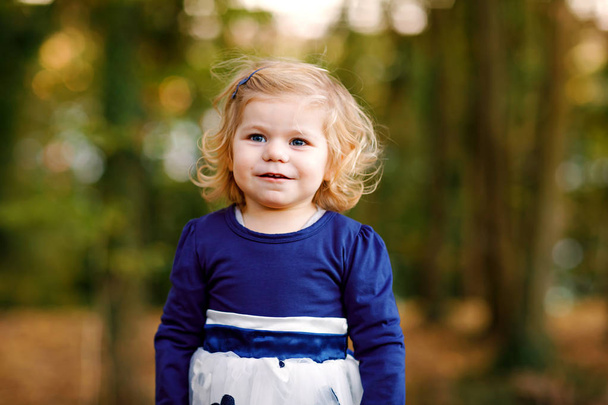 Aranyos kis tipegő lány így egy sétára, őszi parkon keresztül. Boldog egészséges baba élvezi, séta a szülők. Napos meleg őszi napon a gyermek. Aktív szabadidő és a tevékenység a gyerekekkel a természetben. - Fotó, kép