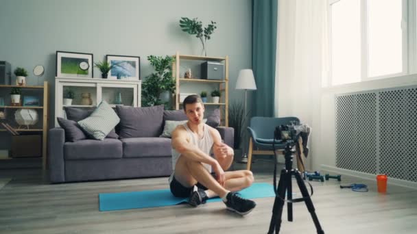 Male blogger recording video on camera talking then exercising abs at home on mat - Footage, Video