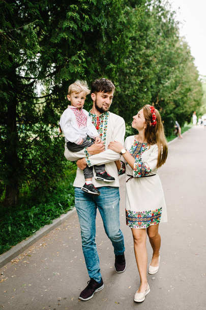 Young family with son in embroidery shirts walking and having fun in green summer park  - Valokuva, kuva