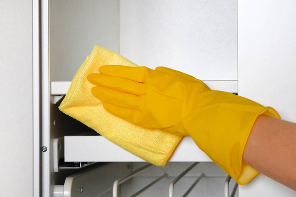 La casalinga che indossa guanti protettivi sta facendo i lavori domestici. Mano in guanto protettivo giallo sta pulendo mobili bianchi con straccio
. - Foto, immagini