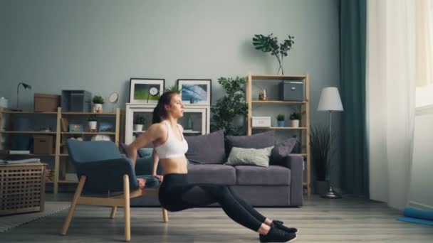 Fit young woman doing pushup dips holding armchair working out in apartment - Filmagem, Vídeo