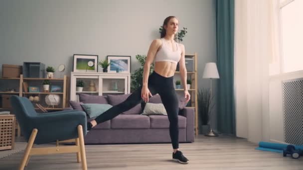Beautiful young sportswoman doing squats at home using armchair training body - Video