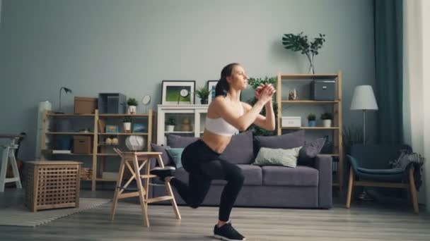 Muscular young woman is doing squats indoors concentrated on physical exercise - Πλάνα, βίντεο