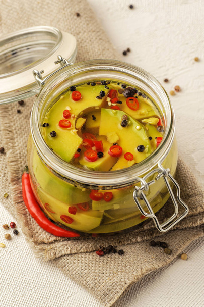 Fermented avocado vegetables with red chili peppers. Glass jar on a light background. Natural linen fabric. - Φωτογραφία, εικόνα