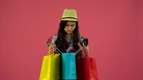 Girl looks into shopping bags then the purse has run out of money but there is a card. Pink background - Materiał filmowy, wideo
