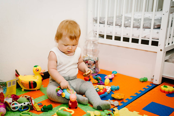 happy little girl eating bagel and playing with toys on colored mat and puzzles - Photo, Image