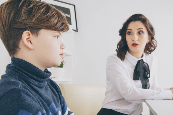 Jonge brunnette vrouw praten met de jongen binnen de witte kamer. Psycholoog vrouw met patiant. Psychologie therapie. - Foto, afbeelding