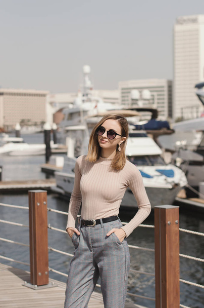 Young european female standing near yachts at pier or marina promenade in a sunny day - Foto, imagen