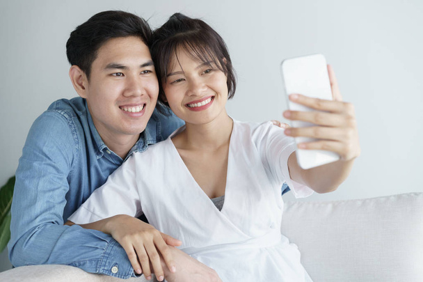 Cute couple in love are hugging and sitting on the sofa,They are selfie in the morning indoors at home - Foto, imagen