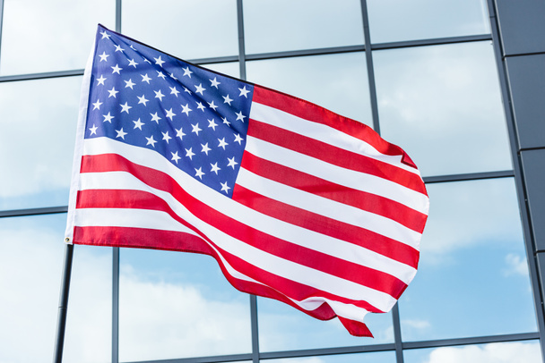stars and stripes on flag of america near building with glass windows and sky reflection - Photo, Image